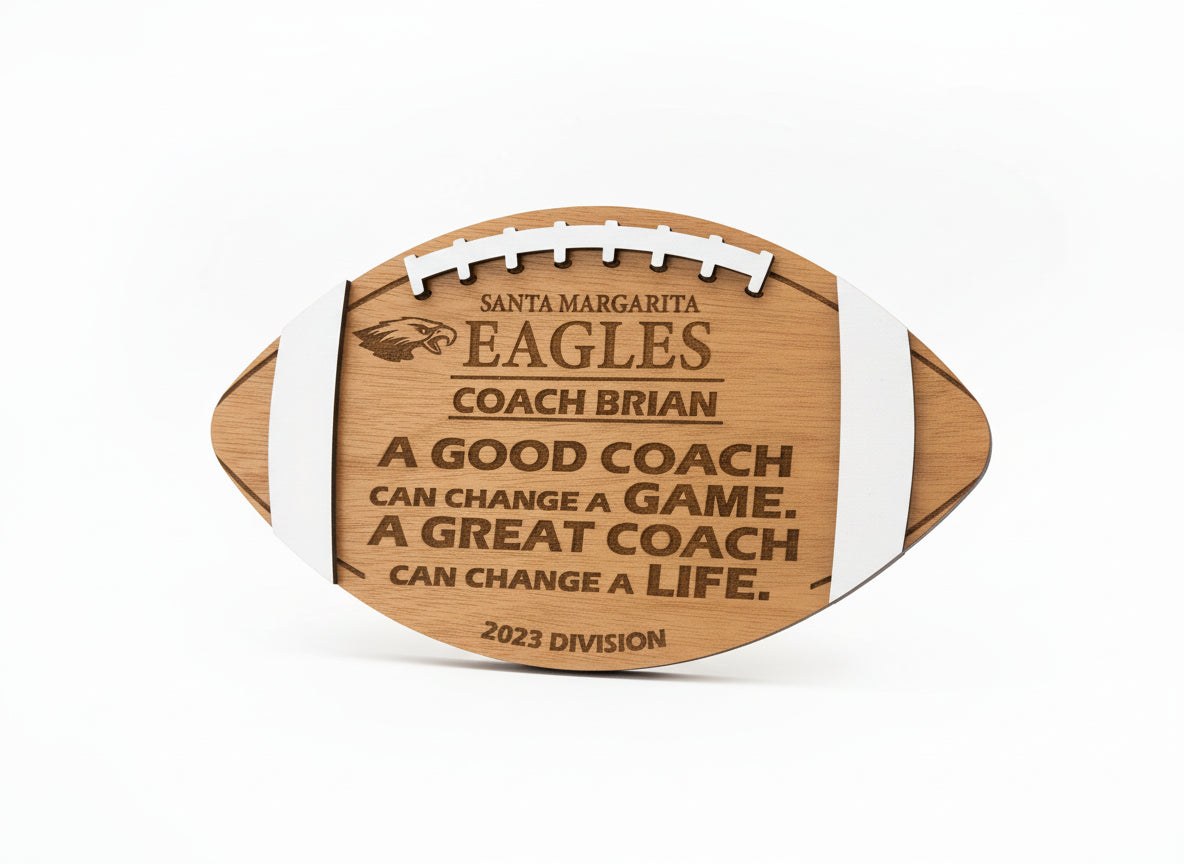 Wooden football-shaped plaque with engraved text on a beige wall.  Cherry wood