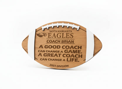 Wooden football-shaped plaque with engraved text on a beige wall.  Cherry wood